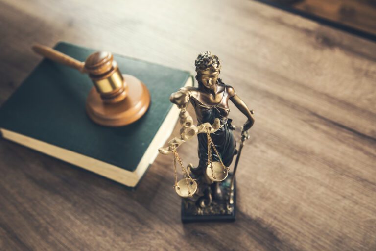 Lady Justice statue with gavel and law book on wooden desk symbolizing legal justice