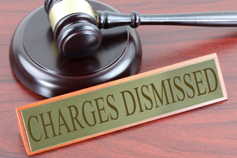 Judge’s gavel beside “charges dismissed” sign on courtroom desk, legal case victory