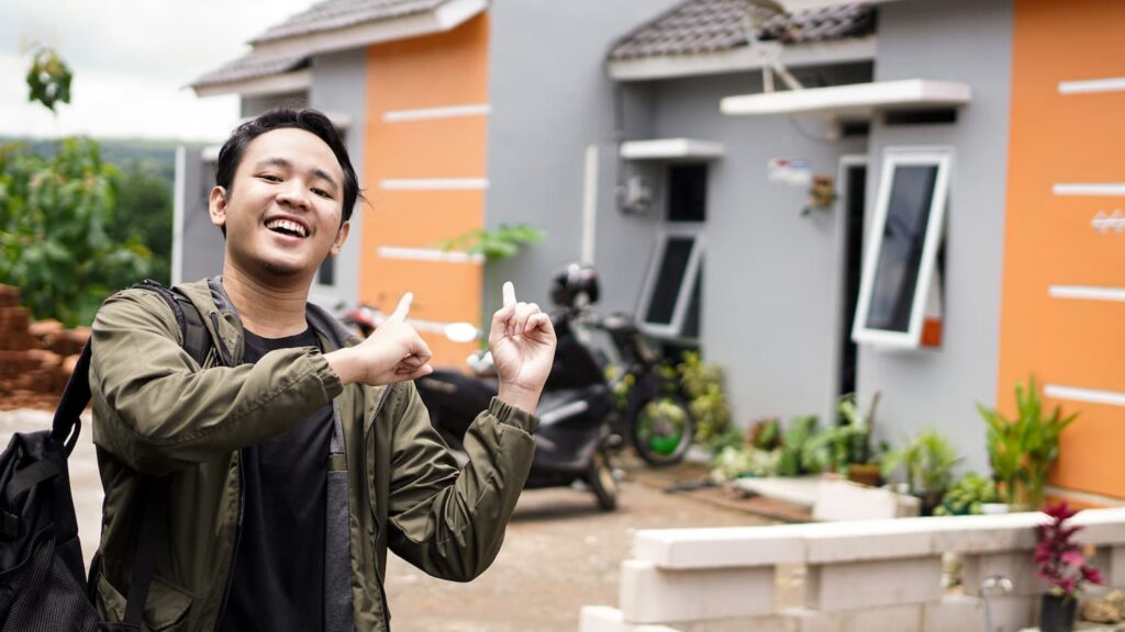 Smiling man pointing toward a small modern house exterior