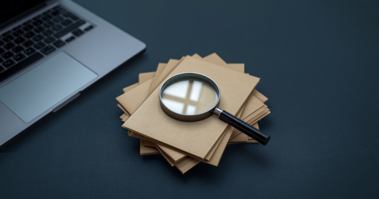 Magnifying glass resting on a stack of tan folders beside a laptop